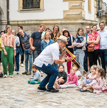 Jazzweekend © Dominik Hupf Posaunist spielt vor einer Reihe Kinder, die auf dem Boden sitzen. Um die Szene sind stehende Menschen versammelt.