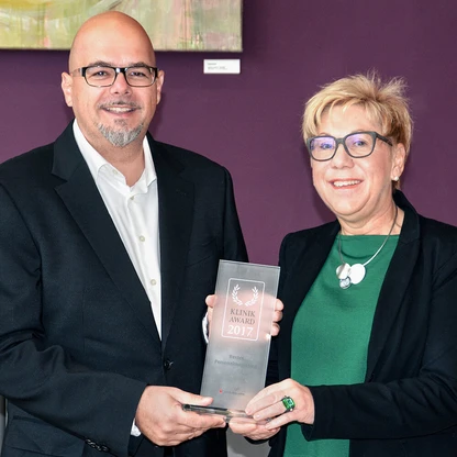 Ein Mann und eine Frau halten gemeinsam einen Preis in die Kamera.